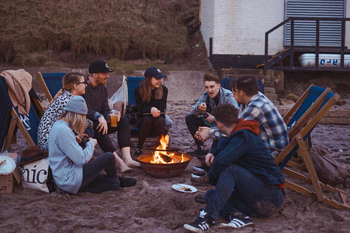 Grupo de amigos sentados alrededor de una fogata en la playa. 