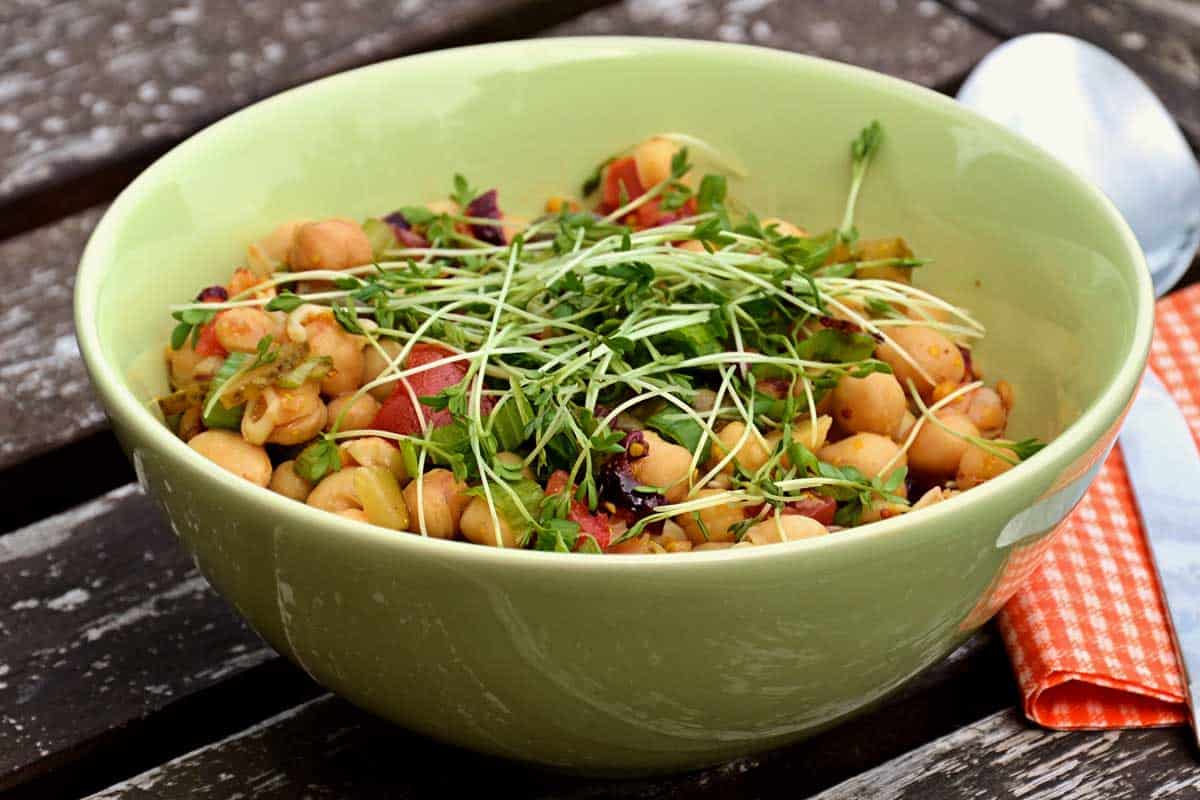 Green bowl with chickpea salad on a picnic table. 