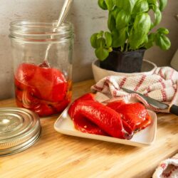 Roasted red peppers on a kitchen countertop, with some on a plate and others in a jar.