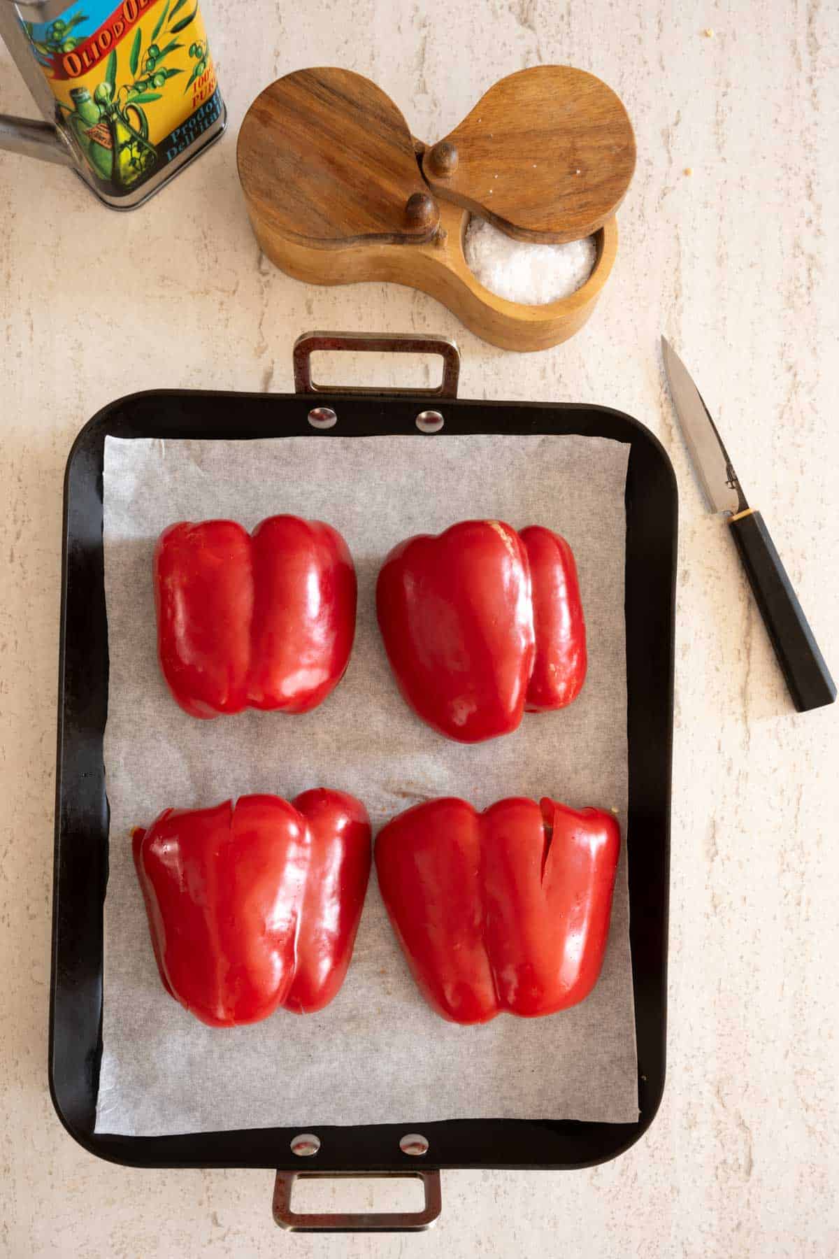 Four red bell peppers cut in half on a parchment-lined baking tray.