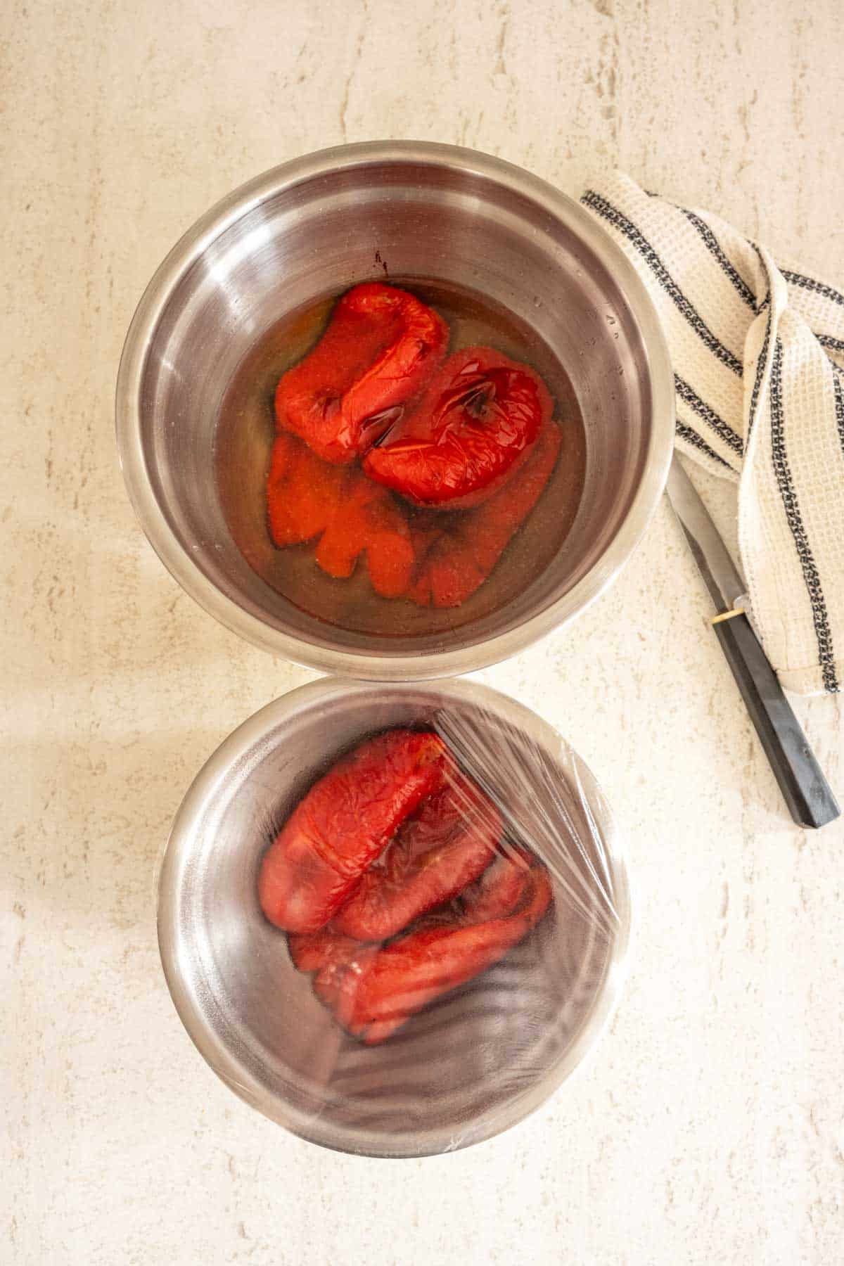 Two stainless steel bowls on a countertop containing roasted red peppers.
