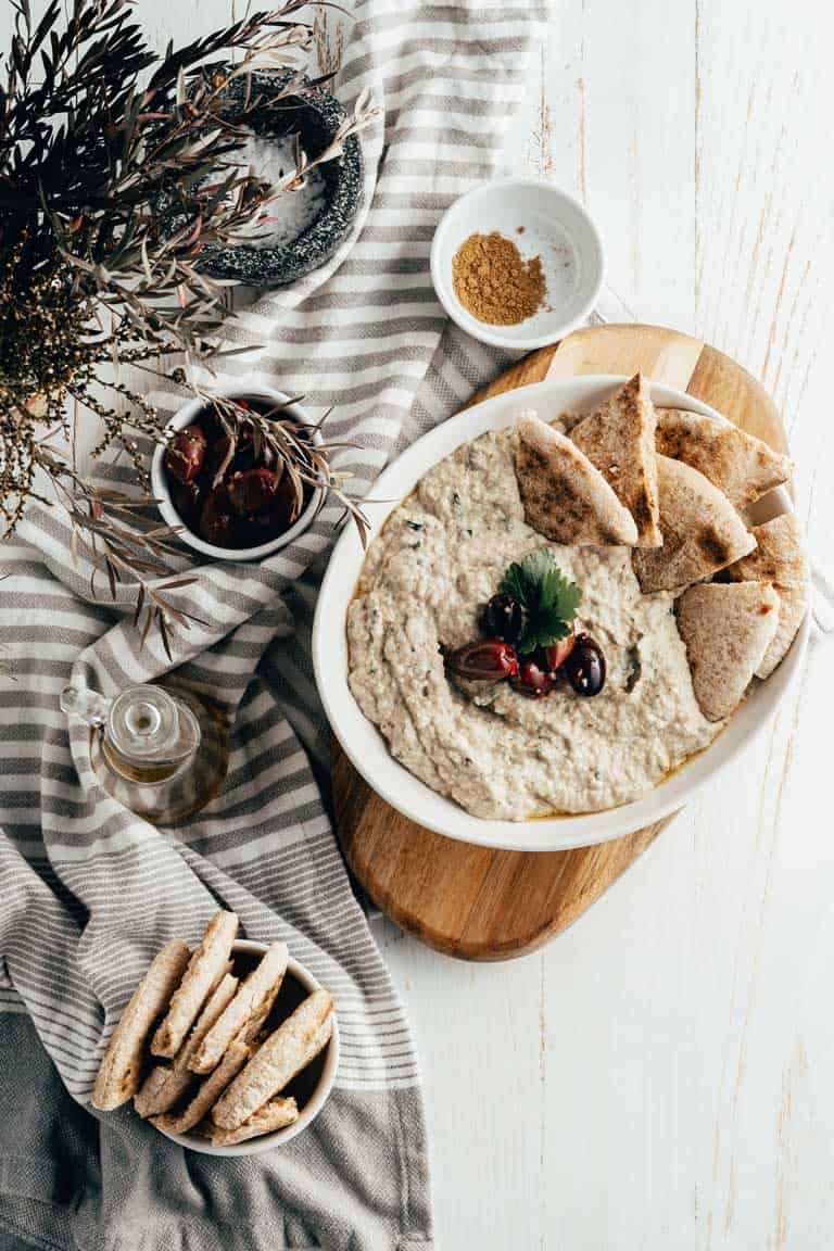 Bowl of eggplant babba ganoush dip with pita breads and olives. 