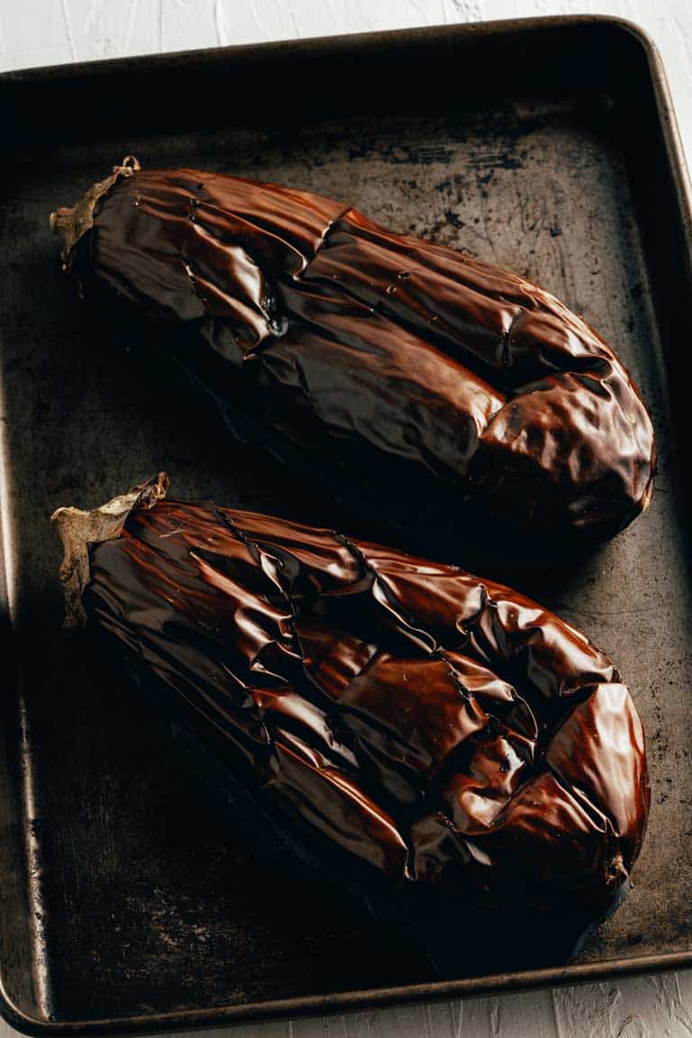 Whole wrinkled eggplants on a tray after roasting.