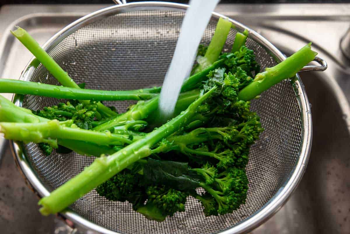 Florets of broccoli being rinsed under running water in a colander. 