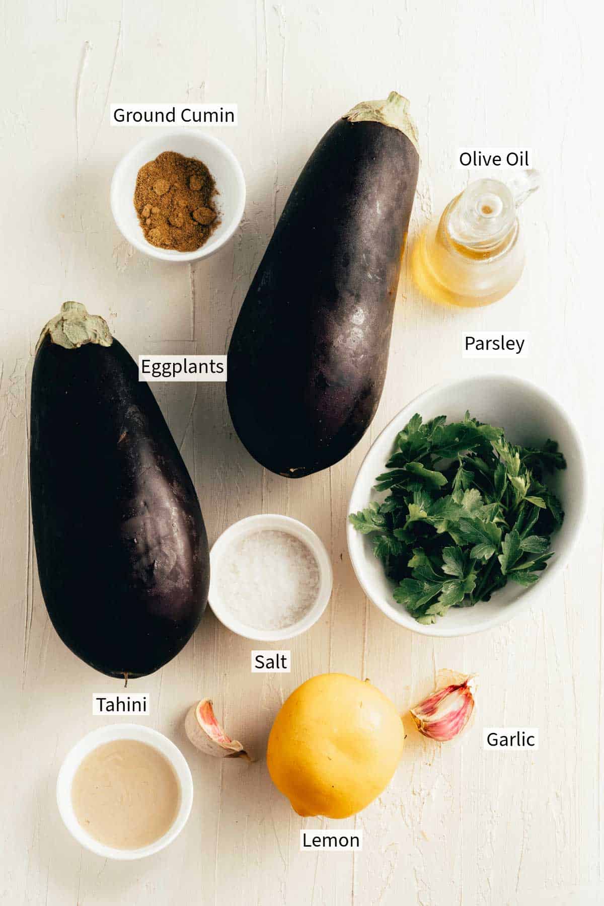 Ingredients for eggplant dip are arranged on a white surface.