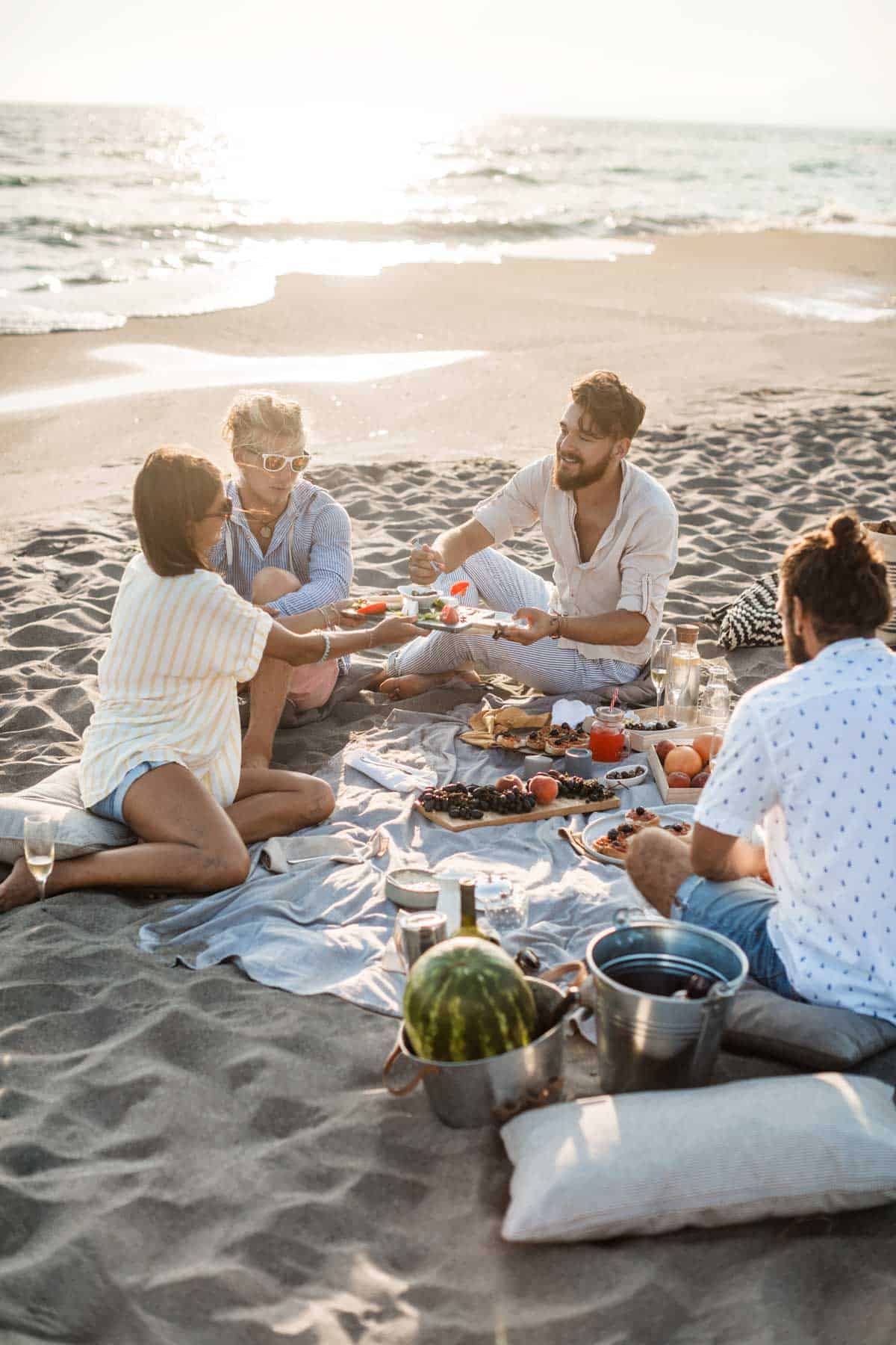 Friends enjoying a picnic on the beach at sunset. 