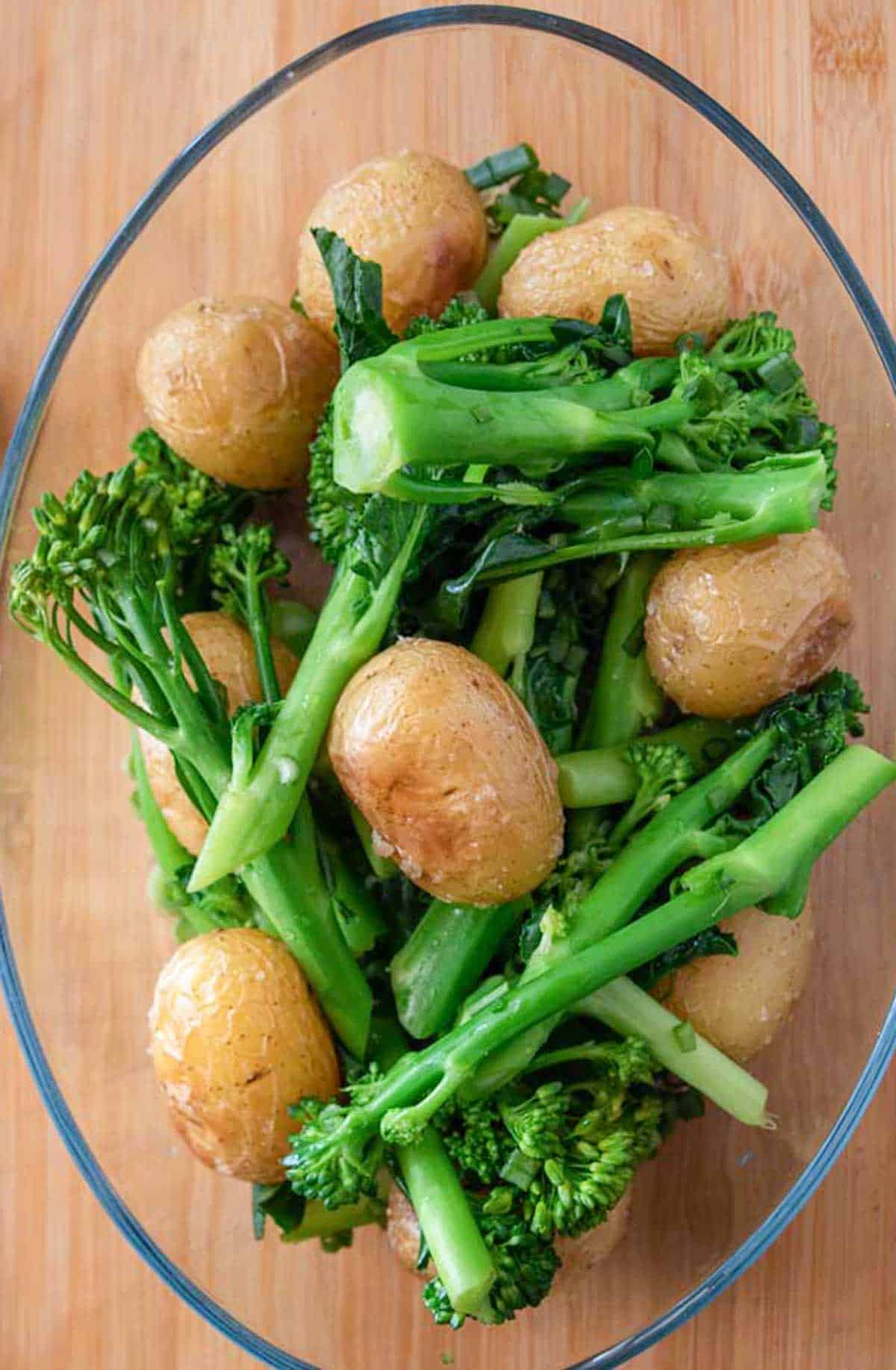 A bowl of broccoli and potatoes on a wooden table.