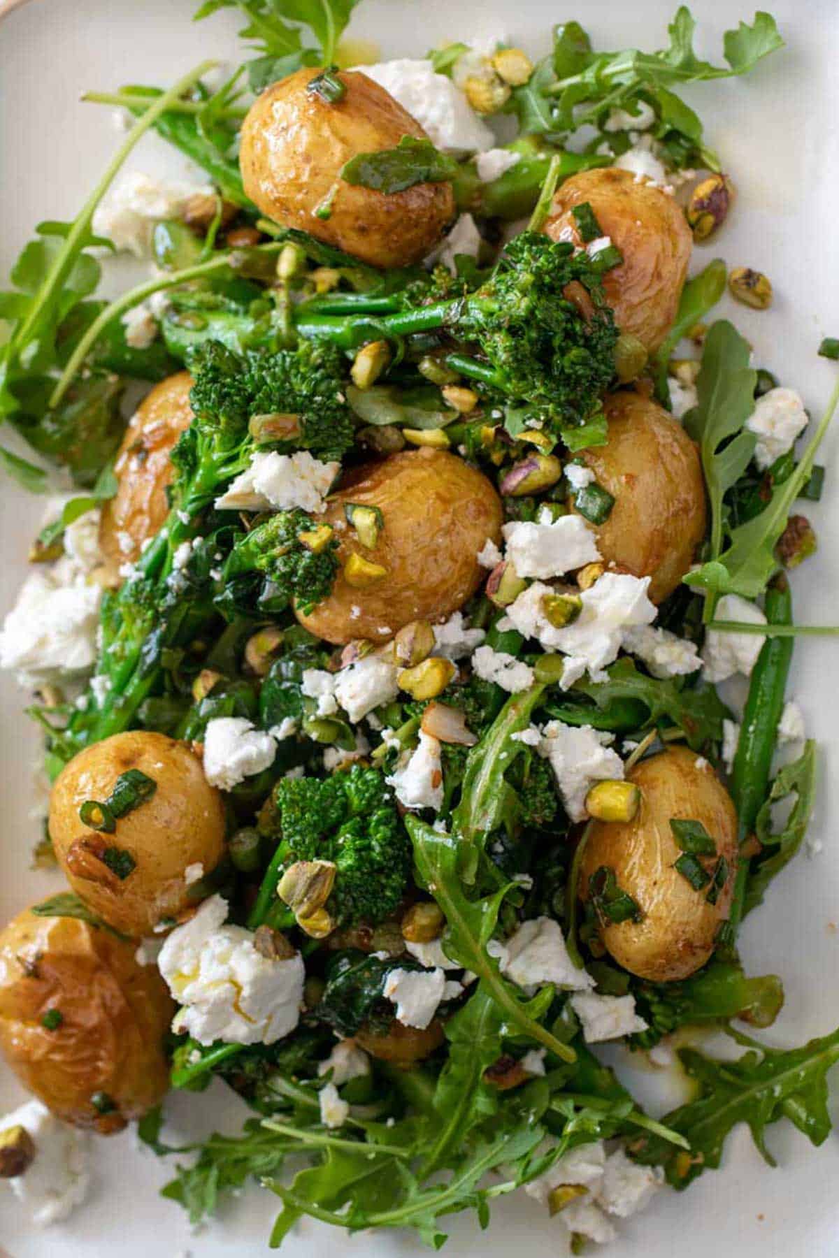 A plate with broccoli potato salad topped with feta and nuts.