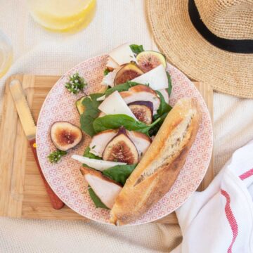 Chicken, fig and goat cheese salad baguette on a plate next to a straw hat.