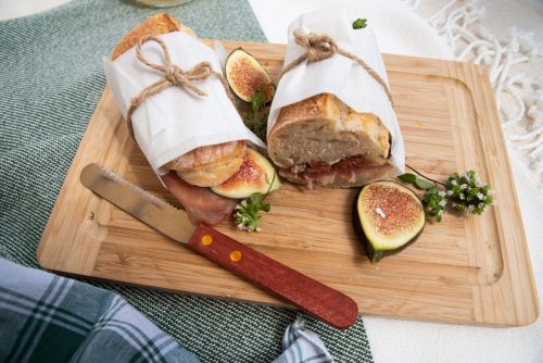 A fig and prosciutto baguette cut in two and wrapped in paper.