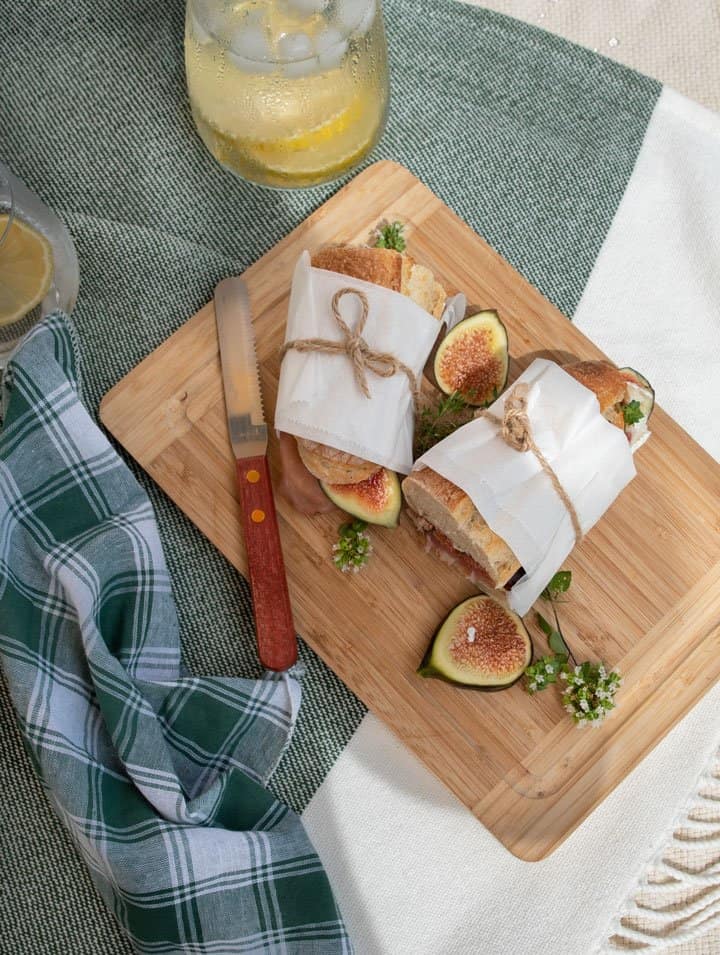 Fig and prosciutto baguette sandwich cut in half and wrapped in paper tied with string on a wooden board.