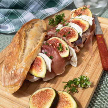 Fig and prosciutto baguette sandwich on a wooden cutting board.