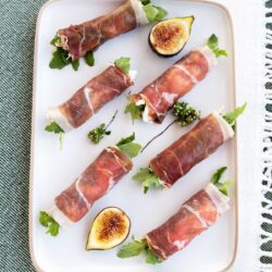 Figs wrapped in prosciutto on a white plate.