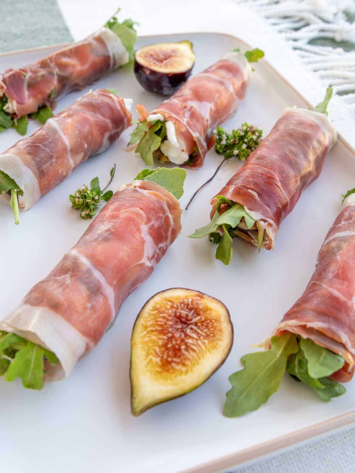 Prosciutto wrapped figs on a white plate with fig quarters for garnish