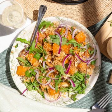 A plate of pumpkin salad with arugula, quinoa, red onion, and roasted butternut squash.