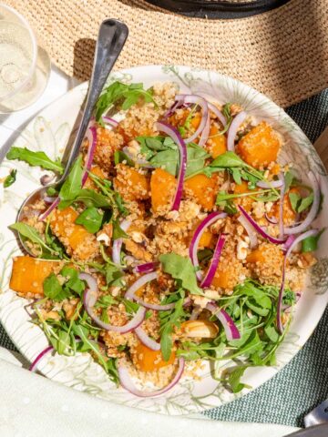 A plate of pumpkin salad with arugula, quinoa, red onion, and roasted butternut squash.