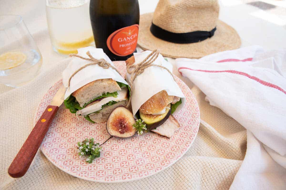 Chicken and fig baguette wrapped in paper tied with string at a picnic. 