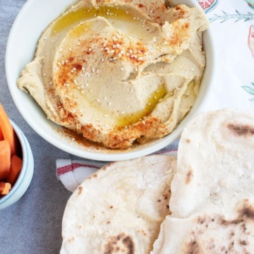 Bowl of homemade hummus with carrot sticks and flatbread.