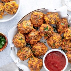 A bowl of cooked meatballs garnished with herbs, some placed on a separate plate. A small dish of red dipping sauce is beside the bowl.