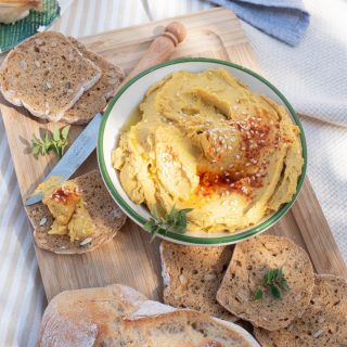 Bowl of pumpkin hummus on a picnic spread with bread.