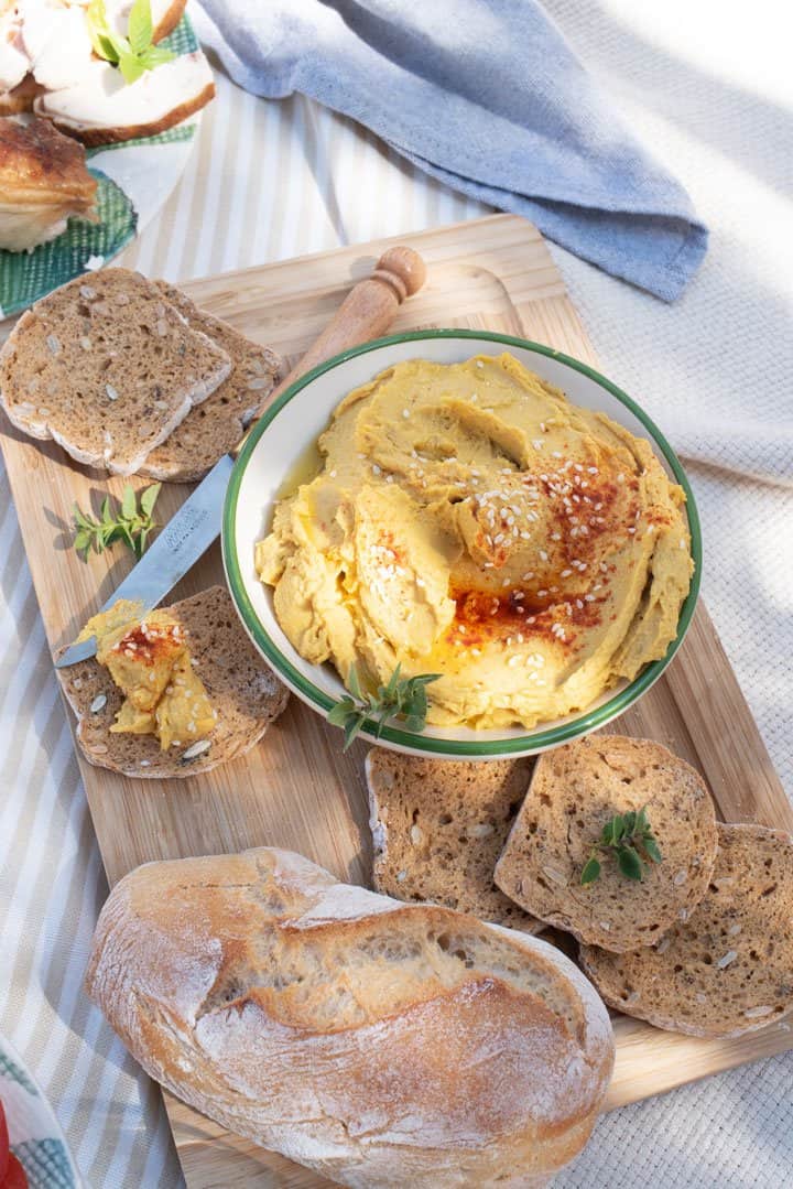 Bowl of pumpkin hummus on a picnic spread with bread.