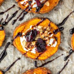 Close-up of a roasted sweet potato slice topped with goat cheese, nuts, and dried cranberries, drizzled with balsamic glaze.