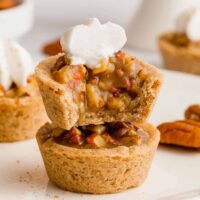 Two pecan pie bites stacked on top of each other, topped with a dollop of whipped cream, placed on a white plate.