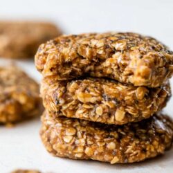 Three stacked oatmeal cookies sit in focus in the foreground, while two more cookies are blurred in the background.