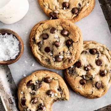 A tray of freshly baked chocolate chip cookies with a side bowl of flaky salt.