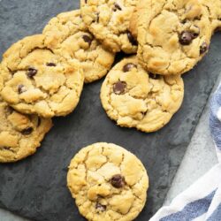 A slate board with several chocolate chip cookies and a cloth napkin on the side.