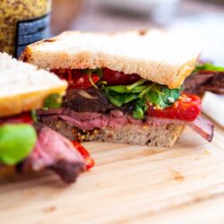 Close-up of a steak sandwich with fresh greens on a wooden board.