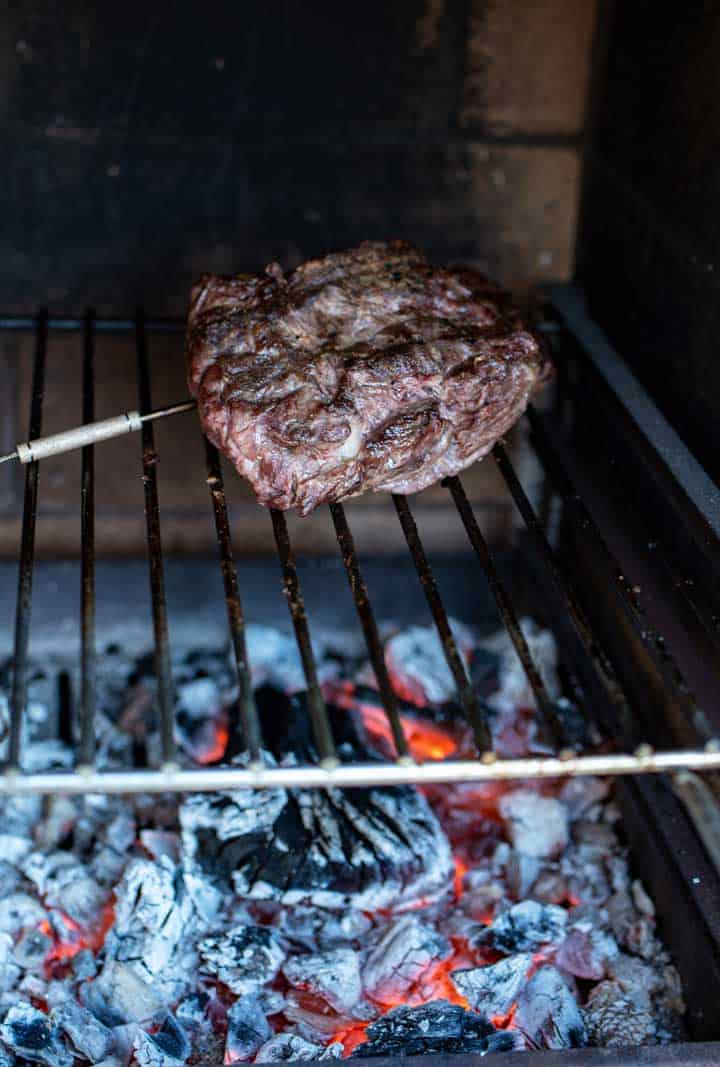 Beef rump grilling over coals with temperature probe inserted. 