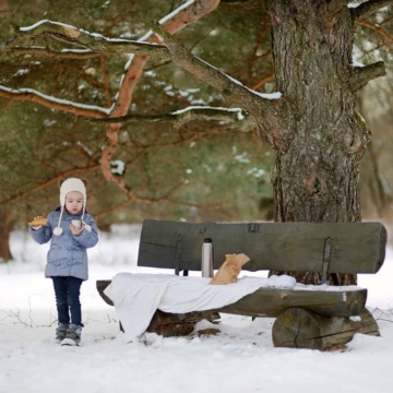Young child in the snow having a picnic lunch on a bench.
