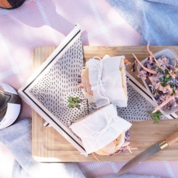 Coleslaw and Baguette sandwich halves wrapped in paper and tied with string on a picnic blanket.