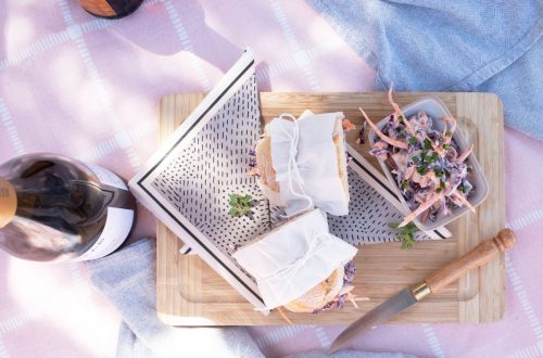 Coleslaw and Baguette sandwich halves wrapped in paper and tied with string on a picnic blanket.