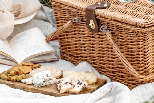 Wicker picninc basket with cheese platter in front.
