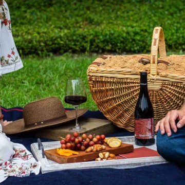 a couple enjoying a picnic on the grass with a classic picnic basket and wine.