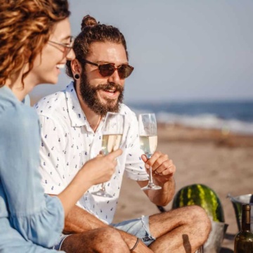 Hip couple enjoying champagne at a beach picnic.
