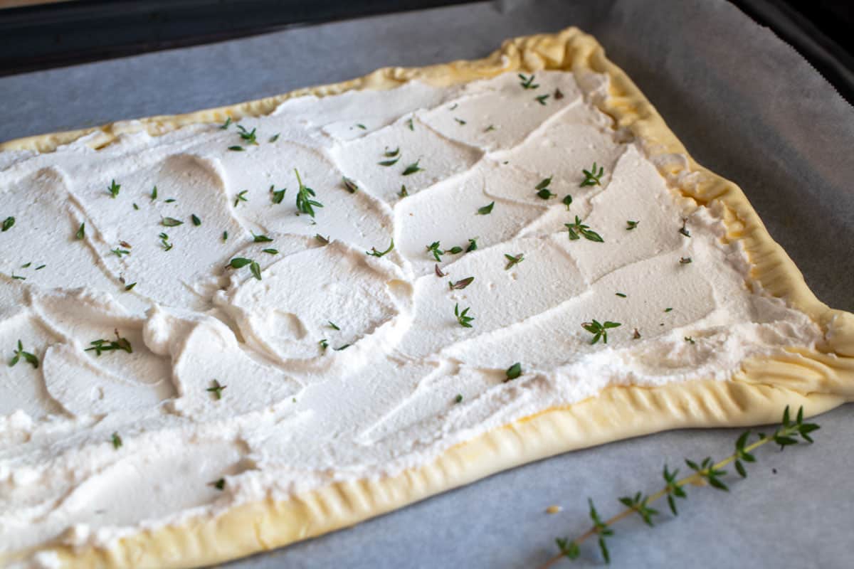 A sheet of pastry with ricotta and thyme on a baking sheet.