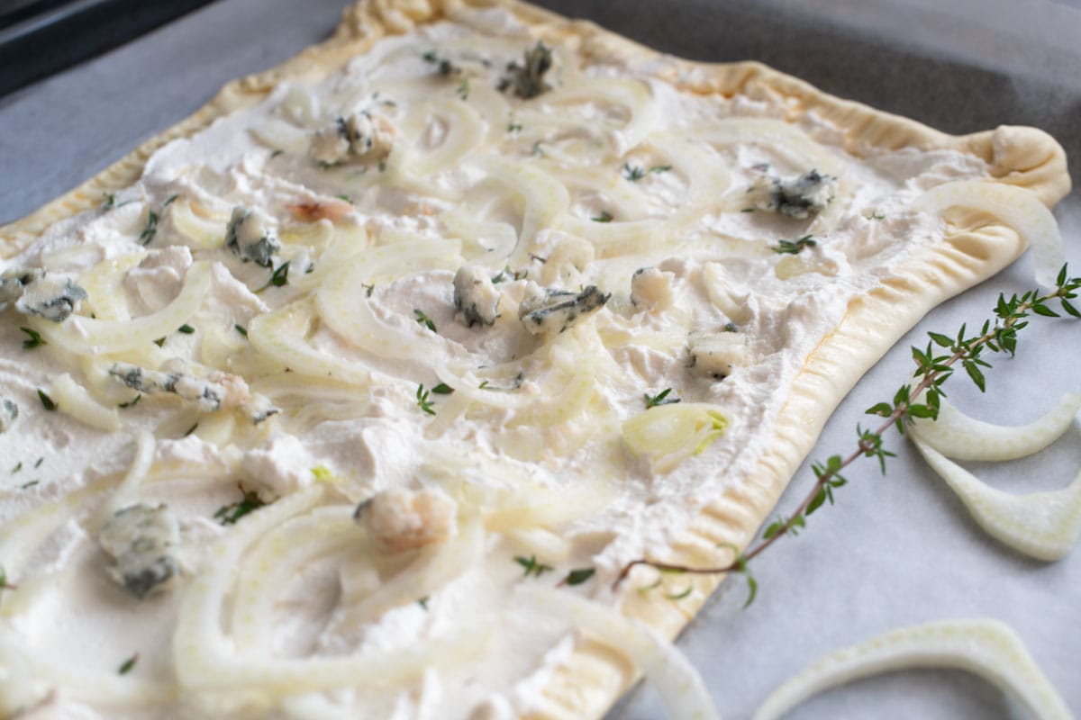 A blue cheese and pear tart on a baking sheet before cooking.