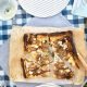 Slices of Pear and ricotta tart on baking paper laid on a blue check picnic table cloth.