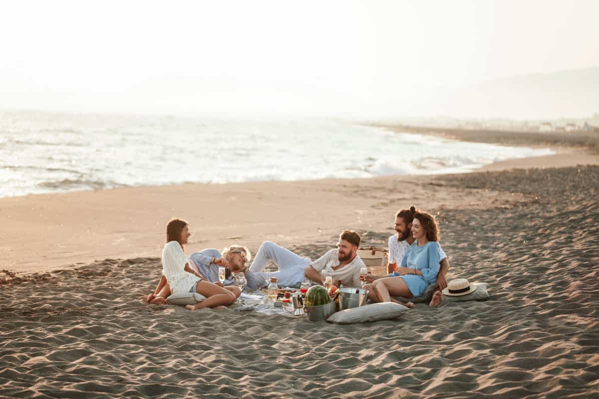 Group of friends enjoying a picnic on the beach at sunset.