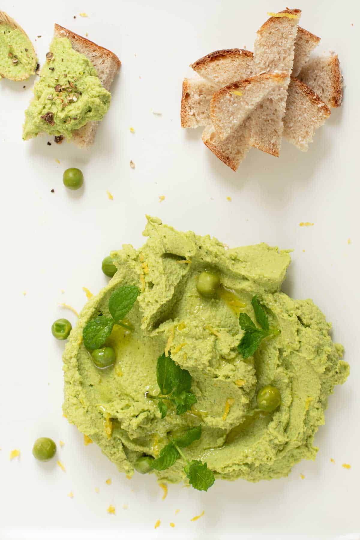 Green pean and mint dip on a plate with pieces of bread.