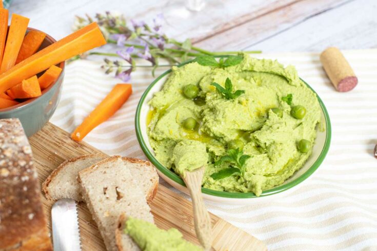 Bright green pean and mint dip on a picnic table with bread and carrots.