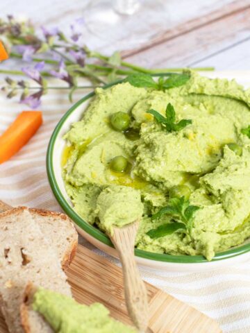 Bright green pean and mint dip on a picnic table with bread and carrots.