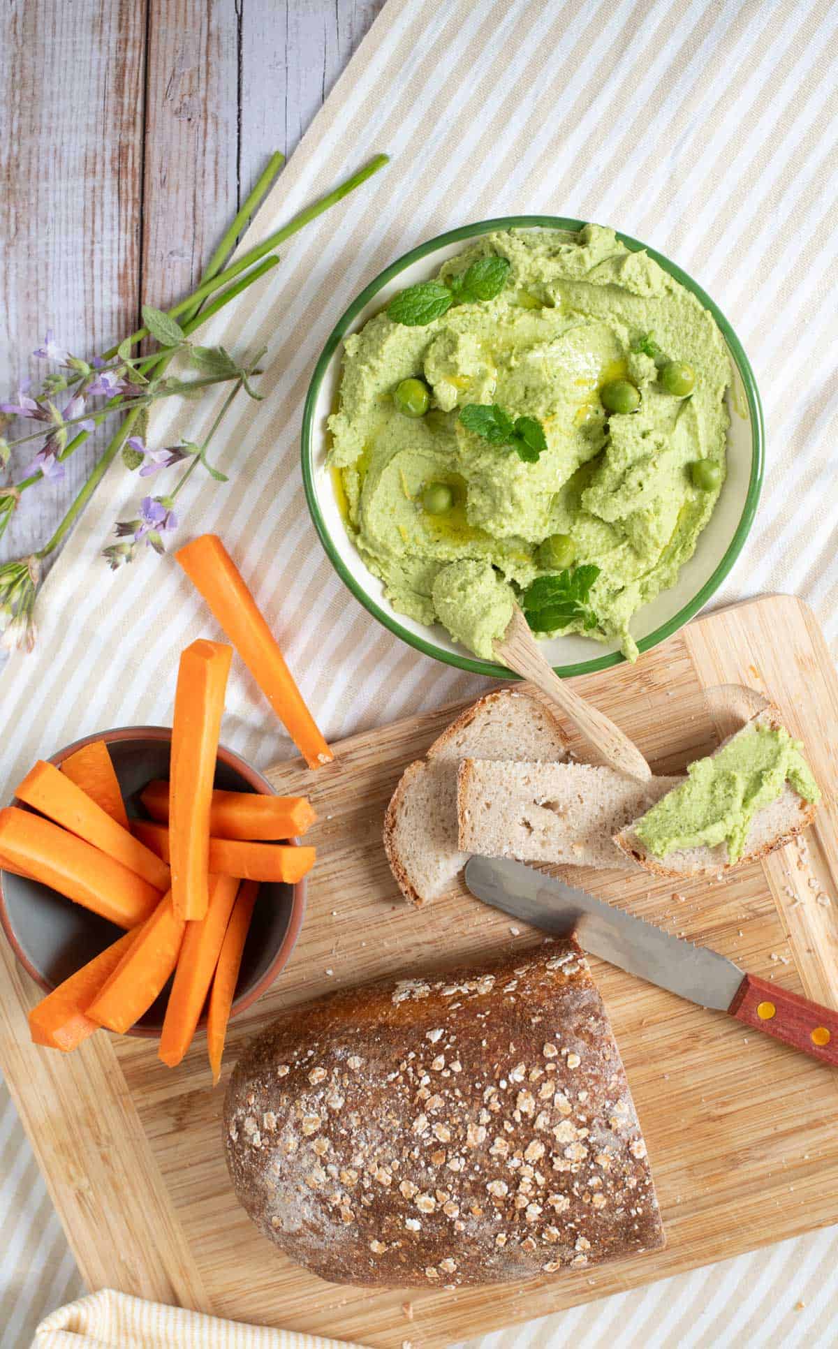 Minty pea dip on a picnic table with a wooden cutting board with bread and carrots sticks. 