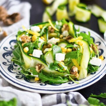 Fresh zucchini ribbon salad, walnuts, corn, and diced cheese served on a decorative plate.