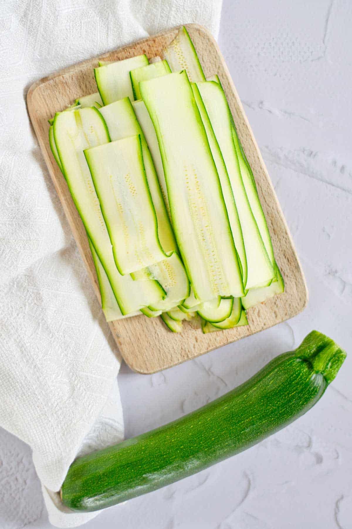 Sliced zucchini arranged on a wooden cutting board next to a whole zucchini.