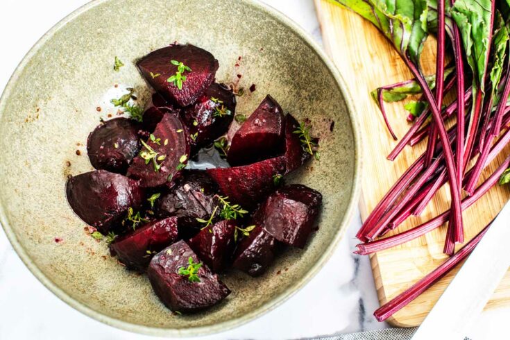 Roasted beets in a bowl with the beetroot leaves scattered around.