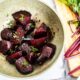 Roasted beets in a bowl with the beetroot leaves scattered around.
